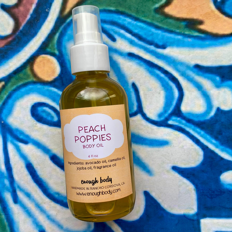 A bottle of Peach Poppies Body Oil with a spray mister, labeled and positioned against a patterned background.