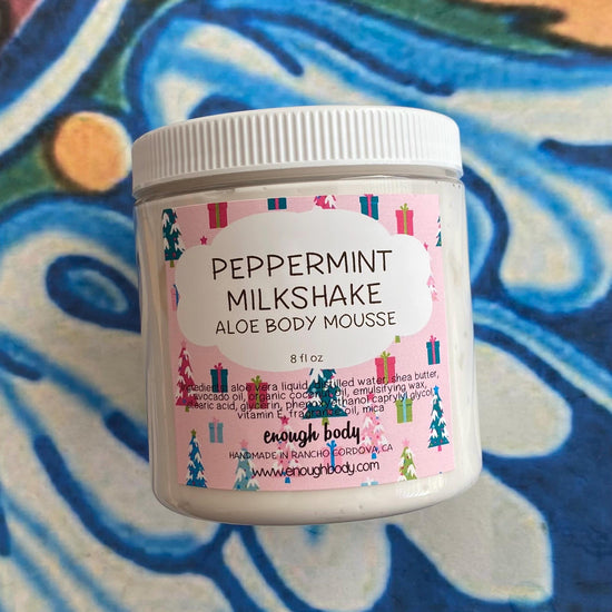 A jar of Peppermint Milkshake Aloe Body Mousse by Enough Body, displayed against a colorful patterned background.