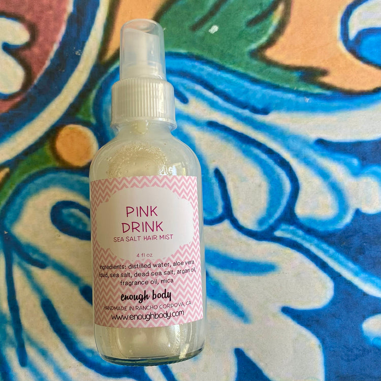 Bottle of 'Pink Drink Sea Salt Hair Mist' on a colorful patterned background