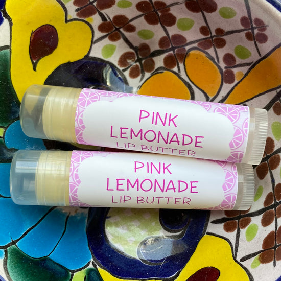 Two lip butter tubes labeled 'Pink Lemonade' on a colorful ceramic plate.