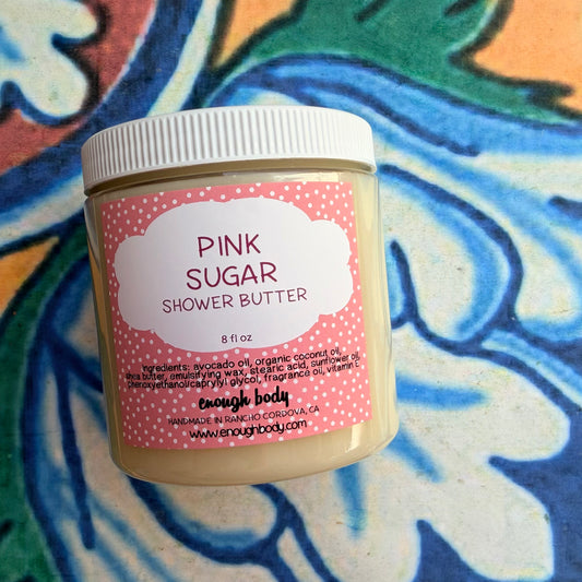 A jar of enough body 'Pink Sugar Shower Butter' with a pink and white label, set against a colorful painted background.