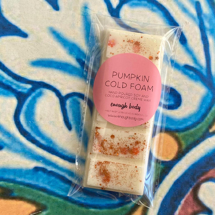 A packaged wax melt snap bar with 'Pumpkin Cold Foam' written on the label, displayed on a colorful patterned background.