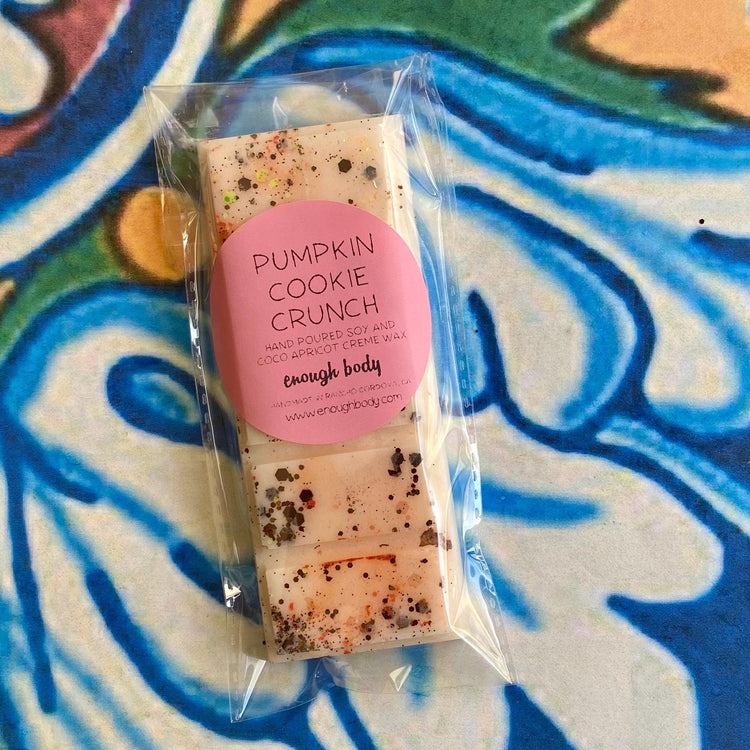 A packaged pumpkin cookie crunch wax melt snap bar with visible glitter on the top surface, placed on a patterned background.
