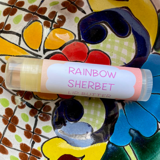 A tube of Rainbow Sherbet Lip Butter placed on a colorful floral background.