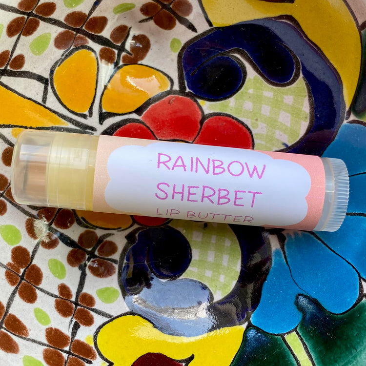 A tube of Rainbow Sherbet Lip Butter placed on a colorful floral background.