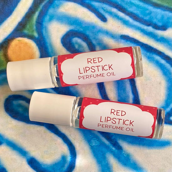 Two glass bottles with a white caps labeled 'red lipstick Perfume Oil' set against a blue, floral patterned background.