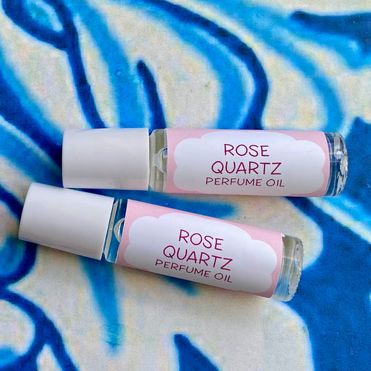 Two glass bottles of Rose Quartz Perfume Oil with white caps and pink labels, displayed against a blue floral background.