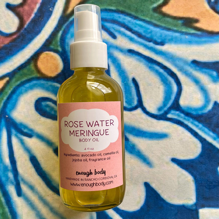 A bottle of Rose Water Meringue Body Oil with a spray mister, labeled and set against a patterned background.