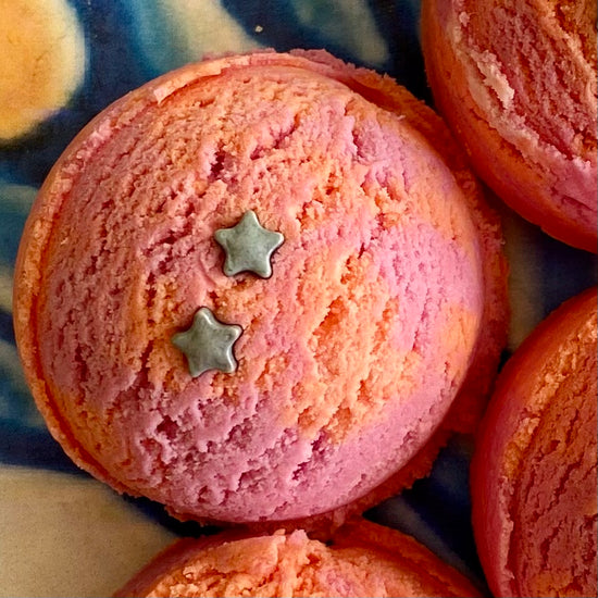 A pink bath bubble scoop with silver star decorations on top, placed on a surface with a reflective background.