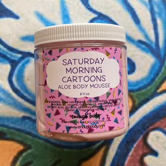 Jar of 'Saturday Morning Cartoons' aloe body mousse with colorful label on a patterned background