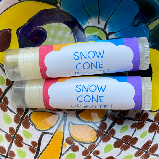 Two tubes of snow cone lip butter on a colorful floral-patterned surface