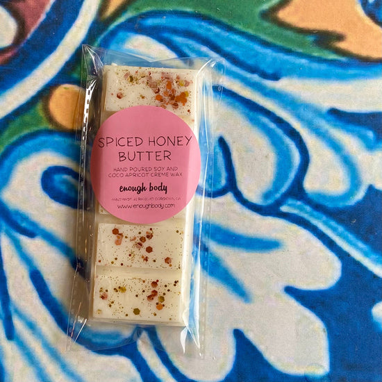 A wax melt snap bar with spiced honey butter label, covered in glitter, placed on a colorful patterned background.