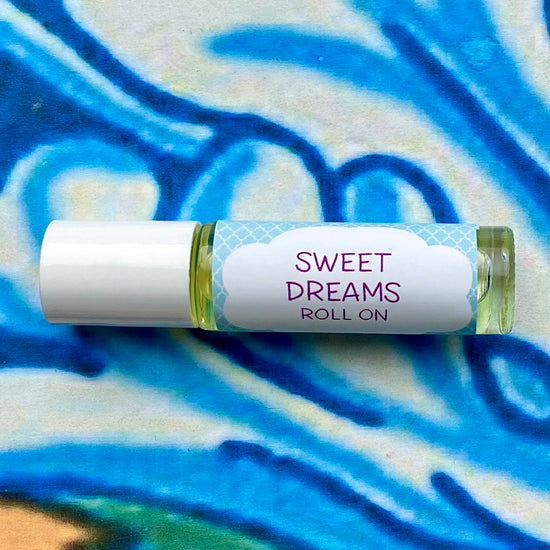 A 10ml roll-on bottle of Sweet Dreams aromatherapy oil with a white cap and label featuring a blue and green pattern. The bottle is placed on a colorful textured background.