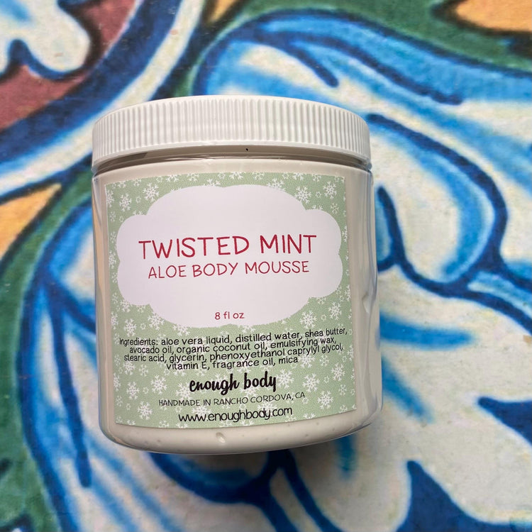 Aloe body mousse jar labeled 'Twisted Mint' on a colorful abstract background