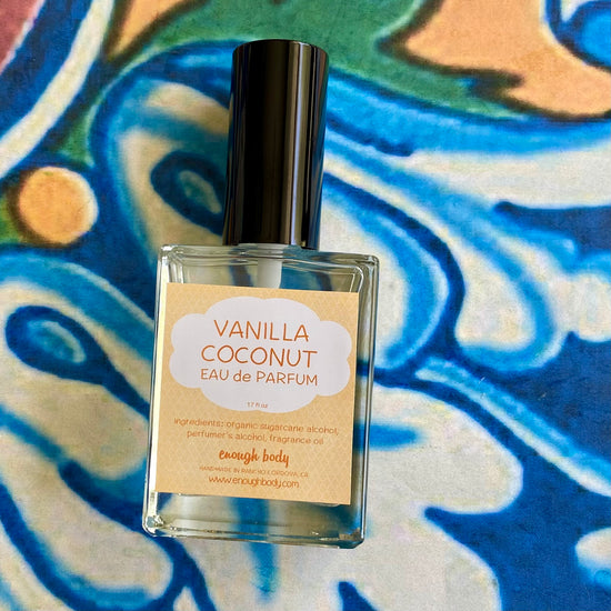 A glass bottle of Vanilla Coconut Eau de Parfum spray with a black spray mister top, labeled on a colorful fabric background.