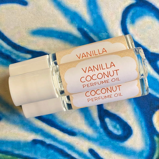 Three glass bottles with a white caps labeled 'vanilla coconut perfume oil' set against a blue, floral patterned background.