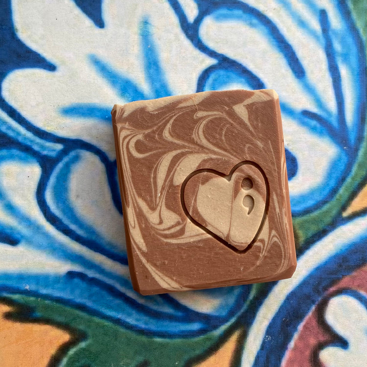 Marbled brown soap with a heart cutout on a colorful tile background
