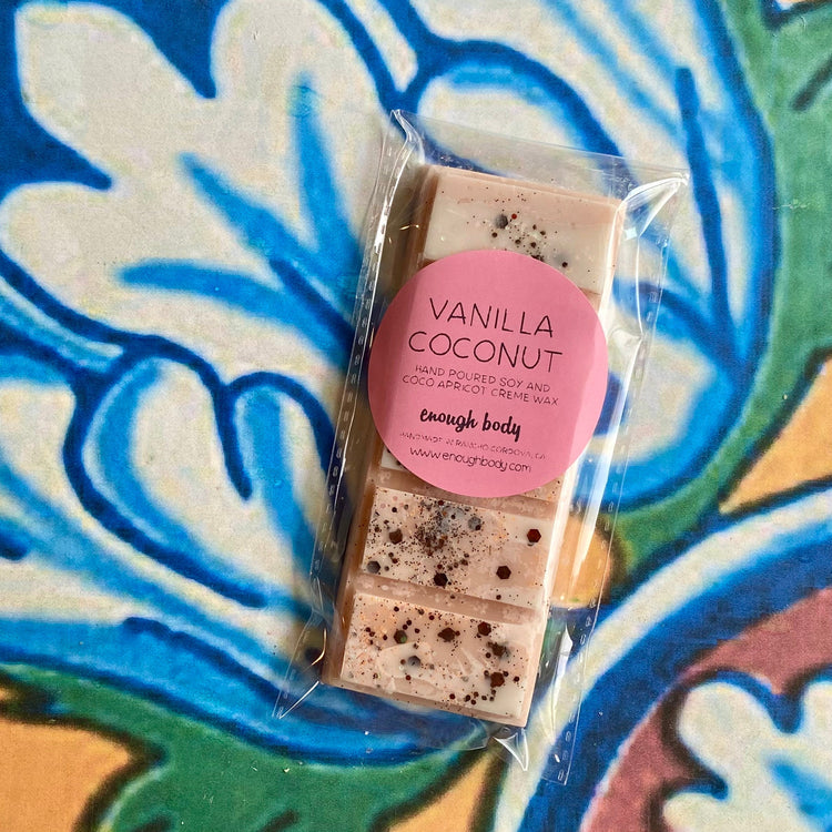A wax melt snap bar with vanilla coconut label, covered in glitter, placed on a colorful patterned background.