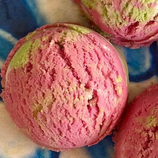 A close-up of a pink and green colored solid bubble bath scoop, with similar scoops visible in the background.