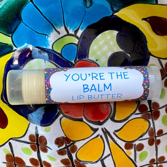 A tube of 'You're the Balm Lip Butter' with a colorful pattern on the packaging and a blue text label.