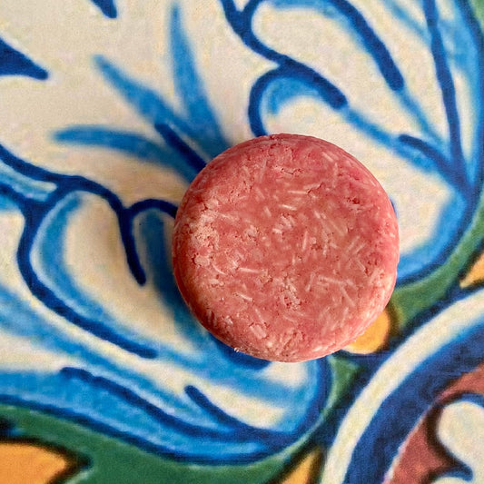 A solid shampoo bar on a patterned background, with a focus on the product's texture and color.