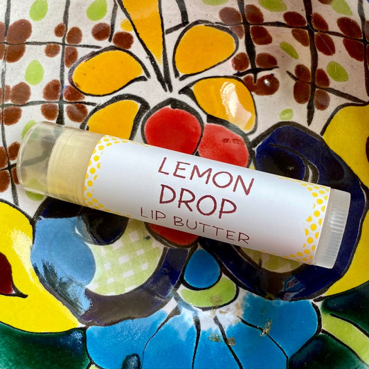 A tube of Lemon Drop Lip Butter placed on a colorful patterned surface.