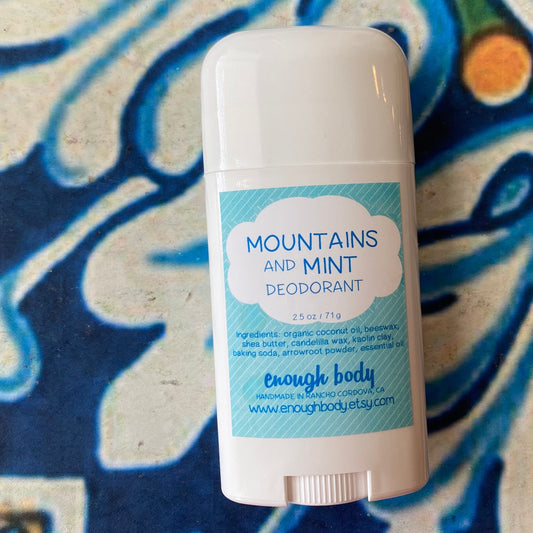 A deodorant stick with a white cap and a label that reads 'Mountains and Mint Deodorant', placed on a decorative background.
