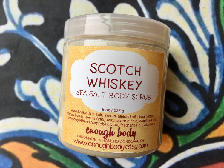 A jar of Scotch Whiskey Sea Salt Body Scrub with a label that includes the product name and a brief description. The jar is on a patterned background.