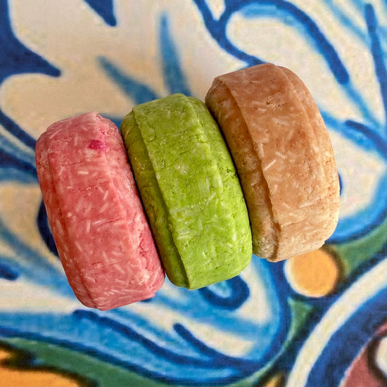 Three solid shampoo bars on a patterned background, with a focus on the product's texture and color.