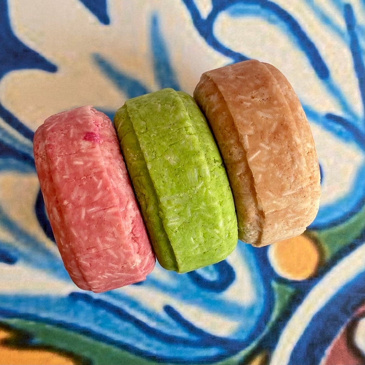 Three solid shampoo bars on a patterned background, with a focus on the product's texture and color.