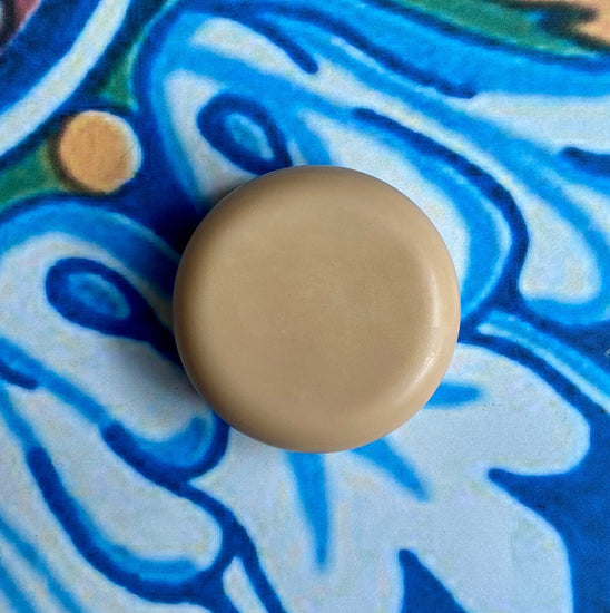 A solid conditioner bar with a vanilla coconut scent, placed on a background with a blue floral pattern.